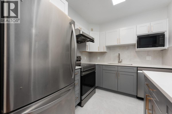 Kitchen with stainless steel appliances, grey and white cabinets, and tile backsplash. - 15 3428 Adanac Street, Vancouver
