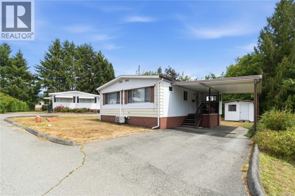Exterior of the mobile home with a carport, shed, and paved driveway. - 15 4935 Broughton St, Port Alberni