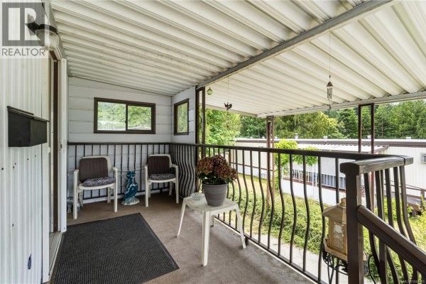 Covered porch with two chairs, a small table with a plant, and metal railings. - 15 4935 Broughton St, Port Alberni