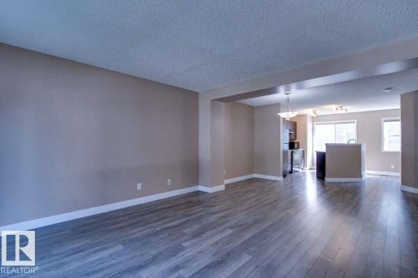 Living room with beige walls and grey laminate flooring, open to the kitchen area. - #15 8304 11 Av Sw, Edmonton