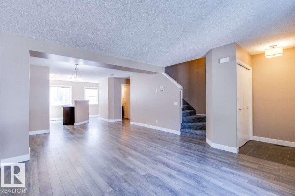 Open-concept living space showing laminate flooring, beige walls, and a carpeted staircase. - #15 8304 11 Av Sw, Edmonton
