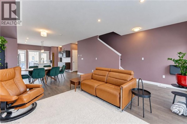 Living and dining area with brown leather sofa, recliner, wood floors, and purple accent wall. - 15 Benninger Drive, Kitchener