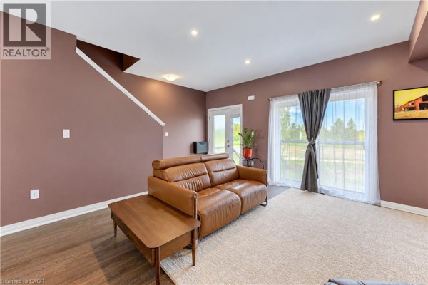 Living area with brown leather sofa, wood coffee table, beige rug, and sliding glass doors to backyard. - 15 Benninger Drive, Kitchener