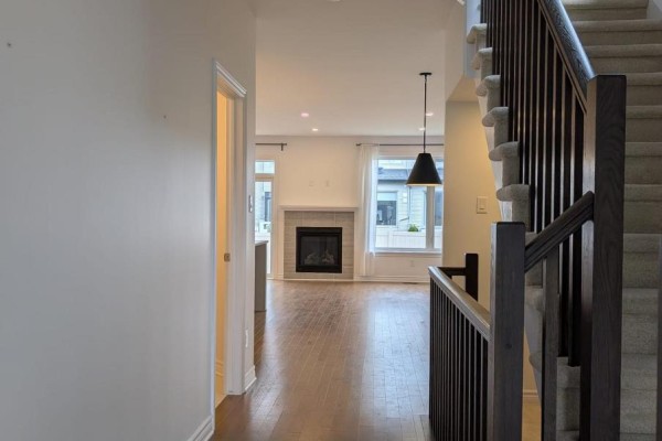 Hallway looking into a living room with a gas fireplace and hardwood floors. - 15 Brixton Way, Ottawa