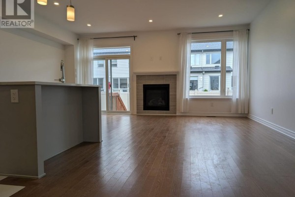 Living room with hardwood floors, a gas fireplace, and large windows. - 15 Brixton Way, Ottawa