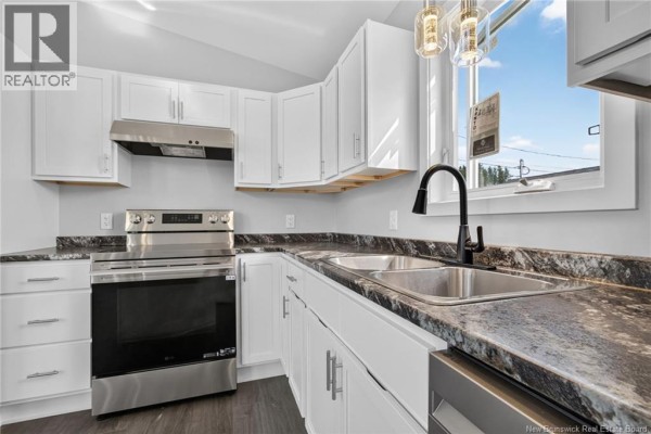Close-up of a kitchen sink and stainless steel dishwasher with dark speckled countertops. - 15 Carolyn Crescent, Moncton