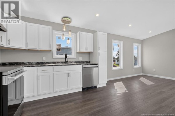 Bright kitchen with white cabinets, stainless steel appliances, and a view of the outdoors through windows. - 15 Carolyn Crescent, Moncton