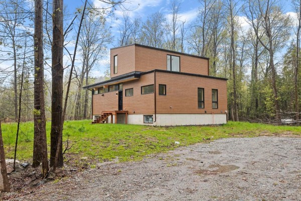 Modern two-story house with brown siding and numerous windows, surrounded by trees. - 15 Ch. Mcgarry, La Peche