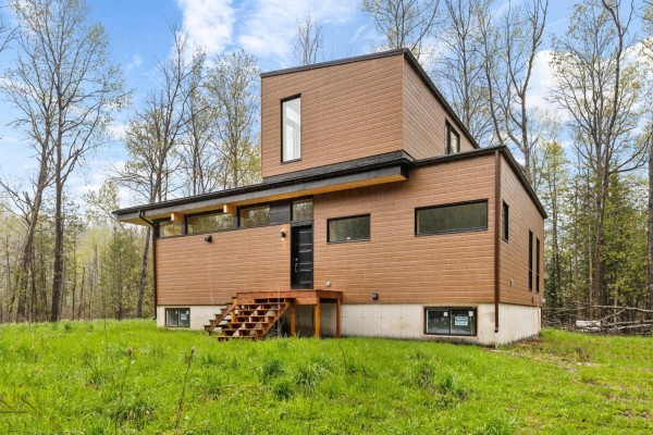 Front view of a modern house with brown horizontal siding and wooden stairs. - 15 Ch. Mcgarry, La Peche