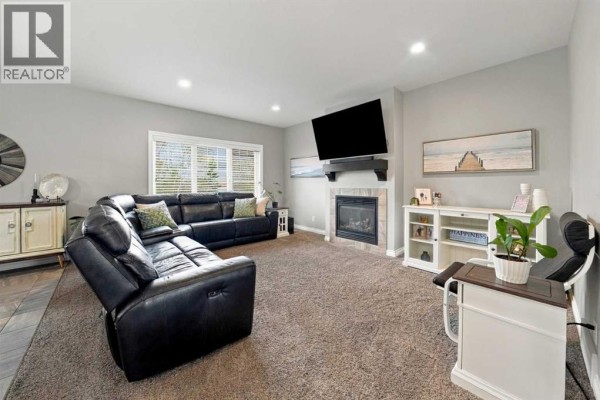 Living room with a black leather sectional sofa, a television, and a gas fireplace. - 15 Cole Way, Sylvan Lake