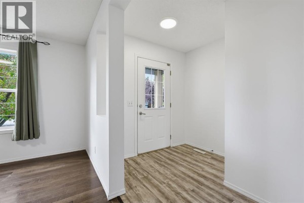 Entryway with a white door, reflective mirror, and gray laminate flooring. - 15 Coventry Link Ne, Calgary