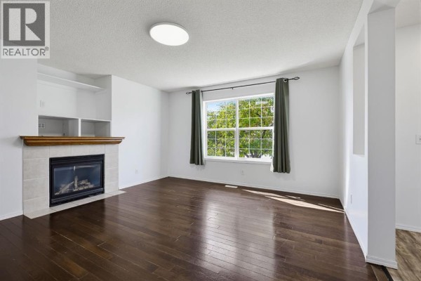Living room featuring a gas fireplace, built-in shelving, and dark hardwood floors. - 15 Coventry Link Ne, Calgary