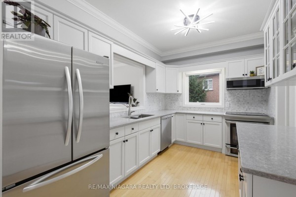 Renovated kitchen with stainless steel appliances, white cabinets, granite counters, and hardwood floors - 15 Cozocar Crescent St Catharines