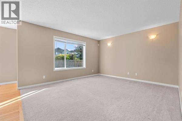 Spacious empty room with beige carpet, light brown walls, and a large window overlooking a backyard. - 15 Cranfield Manor Se, Calgary