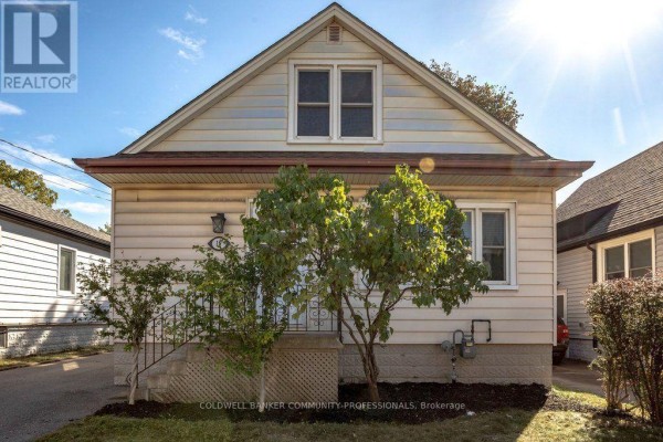 Front view of a light beige house with a green bush in front and a clear sky. - 15 East 27th Street, Hamilton