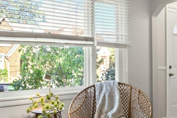 Wicker chair by a window with white blinds and a view of green trees and brick houses. - 15 East 27th Street, Hamilton
