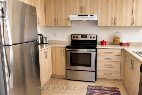 Compact kitchen with light wood cabinetry, stainless steel refrigerator, and black range. - 15 Gower Drive, Aurora