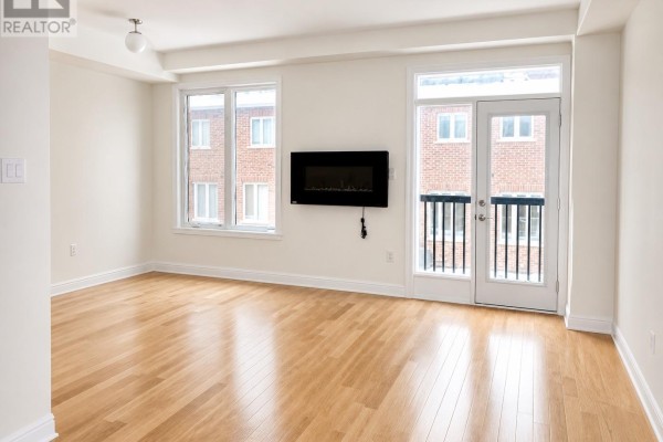 Living room with light wood floors, white walls, electric fireplace, and balcony doors. - 15 Gower Drive, Aurora