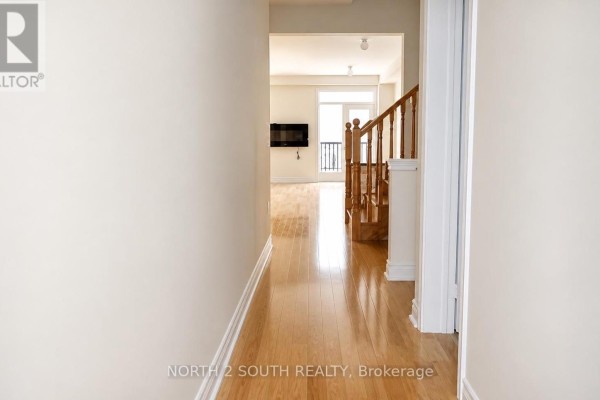 Hallway with wood floors leading to a living area with hardwood floors and staircase. - 15 Gower Drive, Aurora