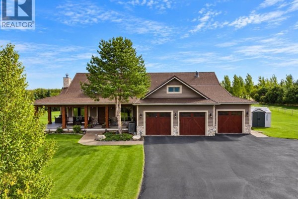 Close-up exterior view of the brown house showing the three-car garage doors and covered porch. - 15 Gray Way, Rural Rocky View County