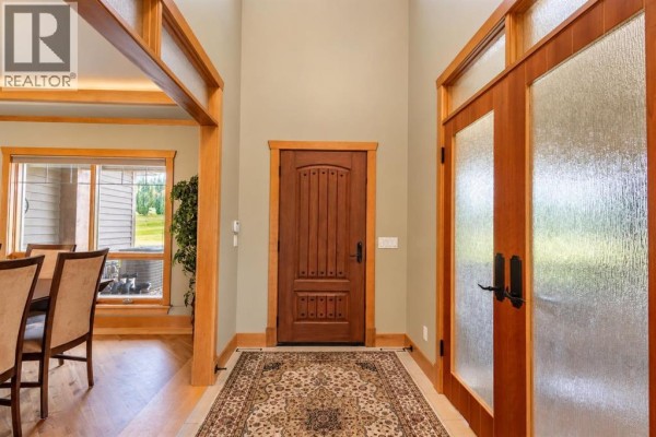 Interior entryway with a wooden front door, glass-paneled side doors, and a patterned rug on the floor. - 15 Gray Way, Rural Rocky View County