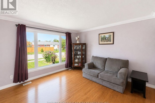 Living room with a gray sofa, a glass display cabinet, and a large window overlooking the front yard. - 15 Gregory Place, St  Thomas