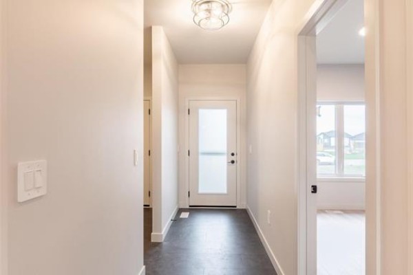 Hallway inside a new home with white walls, dark flooring, and a frosted glass door. - 15 Hester Park Cove, Grande Pointe