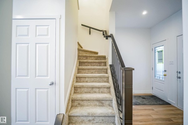 Interior view of a carpeted staircase with a dark brown wooden railing and white doors. - 15 Lemon Cl, Spruce Grove