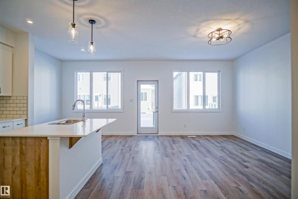 Open concept living area with white walls, wood-look flooring, and a kitchen island with pendant lights. - 15 Lemon Cl, Spruce Grove