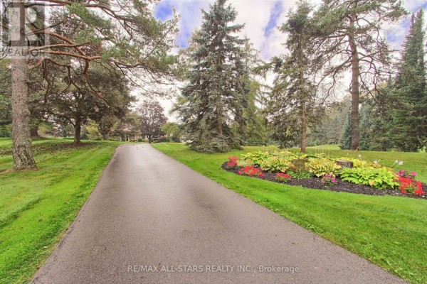 Paved driveway winds through a manicured lawn with mature trees and flower beds. - 15 Lobraico Lane, Whitchurch Stouffville