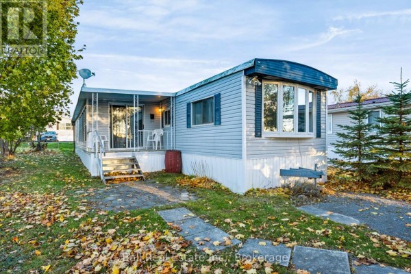Front view of a light blue mobile home with a covered porch and bay window. - 15 Mcgregor Central Drive, Otonabee South Monaghan