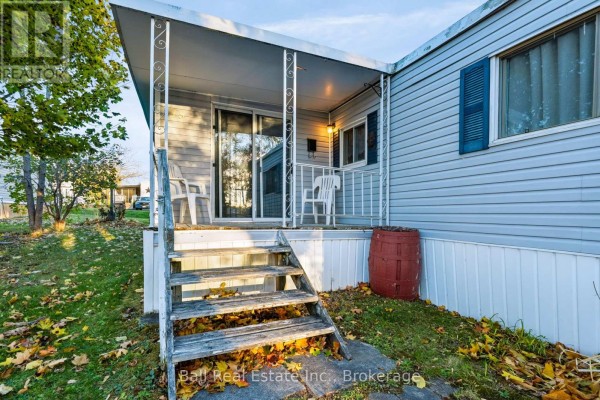 Close-up of the covered porch entrance of a light blue mobile home with wooden steps. - 15 Mcgregor Central Drive, Otonabee South Monaghan