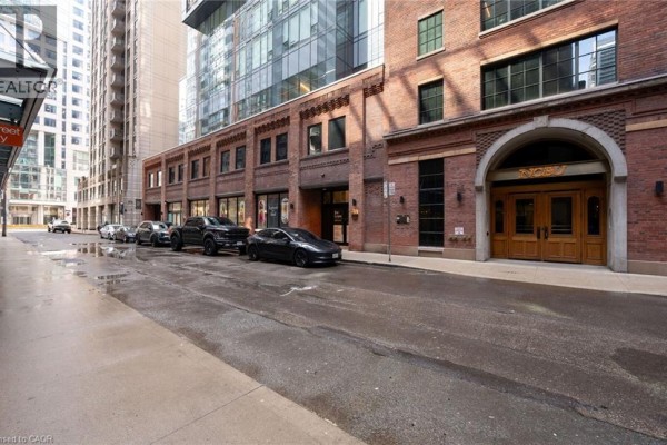 Brick building facade with arched double doors and storefronts, with cars parked outside. - 15 Mercer Street Unit# 620, Toronto