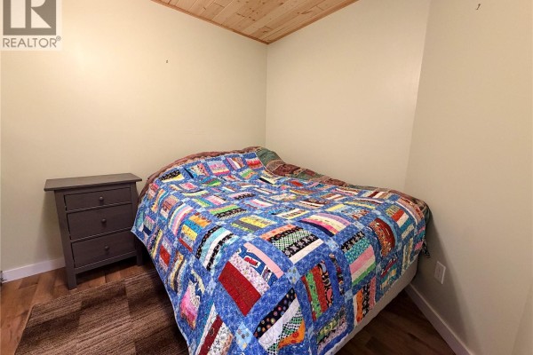 Bedroom with a double bed, colorful quilt, gray nightstand, and wooden ceiling. - 15 Murray Lake Crescent, Murray Lake