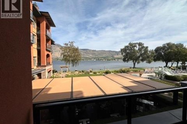 View from balcony overlooking a lake, trees, and resort amenities with mountains in the distance. - 15 Park Place Unit# 209, Osoyoos