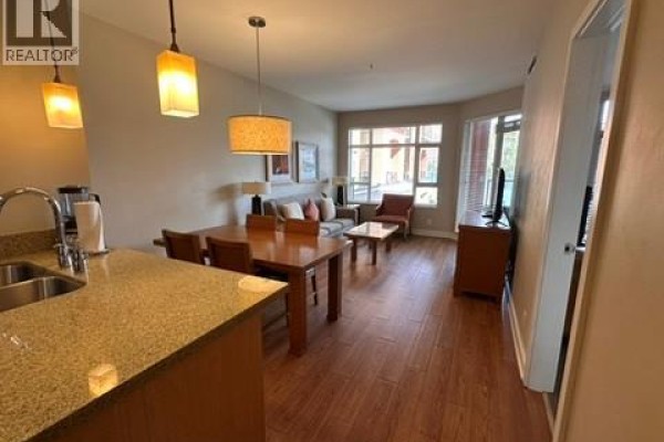 Open-concept living space with dining table, sofas, and large windows overlooking the exterior. - 15 Park Place Unit# 209, Osoyoos
