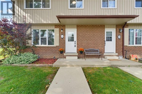 Close-up of the townhouse entrance with brick facade, beige siding, and white doors. - 15 Seneca Street S, Cayuga