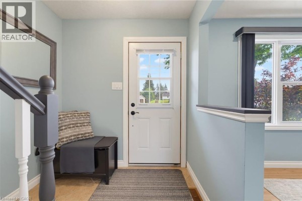 Interior entryway with light blue walls, wood floors, white door, and wooden staircase railing. - 15 Seneca Street S, Cayuga