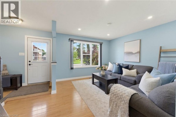 Living room with light blue walls, wood floors, a large window, and a sectional sofa. - 15 Seneca Street S, Cayuga