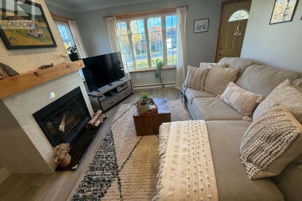 Living room featuring a grey sectional sofa, fireplace with a white surround, and a television on a grey stand. - 15 Spruce Avenue, Happy Valley  Goose Bay