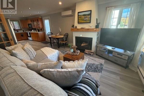 Living room with a sectional sofa, fireplace, television, and dining table and chairs visible in the background. - 15 Spruce Avenue, Happy Valley  Goose Bay