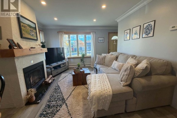 Living room showing a sectional sofa with textured pillows, a fireplace, and large windows with a view of trees. - 15 Spruce Avenue, Happy Valley  Goose Bay