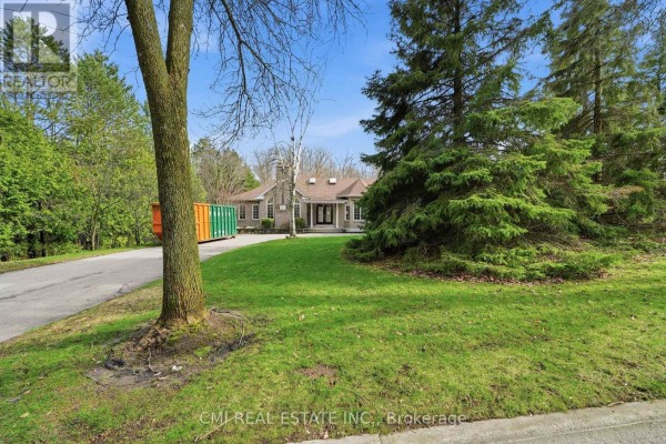 View of a brick bungalow through mature trees and landscaping with green lawn. - 15 Treegrove Circle, Aurora