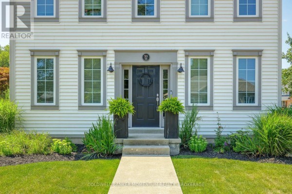 Close-up front view of the entrance to a white house with grey trim, black door, and potted plants. - 15 Virginia Street, Welland