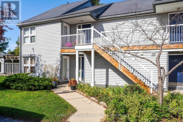 Exterior view of the townhouse building entrance with light grey siding and wooden stairs. - 150 - 53 Trott Boulevard, Collingwood
