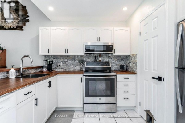Kitchen with white cabinets, stainless steel appliances, wood countertops, and tiled backsplash. - 150 - 53 Trott Boulevard, Collingwood