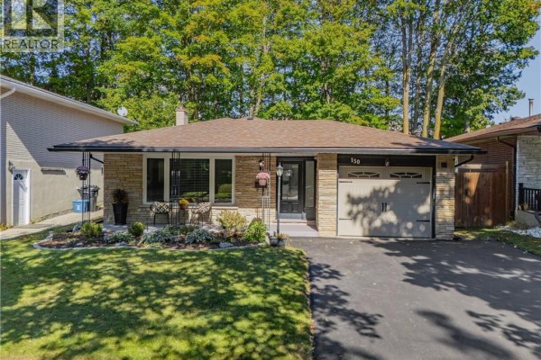 Front view of a bungalow with a lawn, driveway, and trees under a blue sky. - 150 Coach Hill Drive, Kitchener