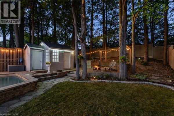 Backyard evening view with a pool, fire pit area, string lights, and shed. - 150 Coach Hill Drive, Kitchener