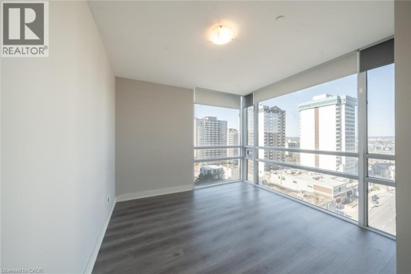 Empty room with grey walls, dark grey flooring, and large corner windows with city views. - 150 Main Street W Unit# Ph3, Hamilton
