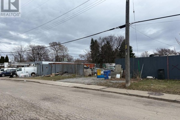 Side view of property with debris and vehicles, showcasing the fenced perimeter. - 150 Princess Street, Hamilton
